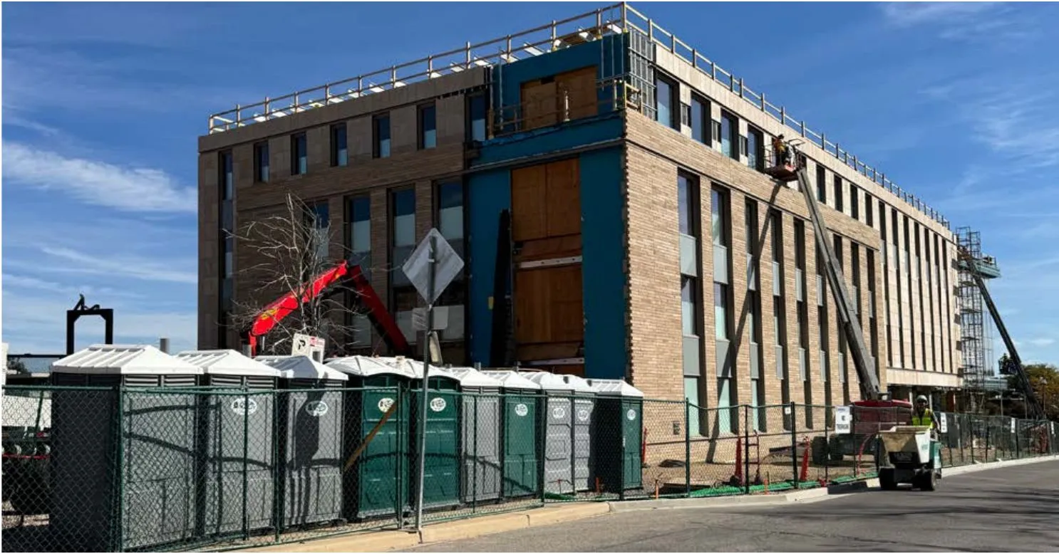 The Western City Campus office building under construction, ringed by a chain-link fence and a row of portable toilets.
